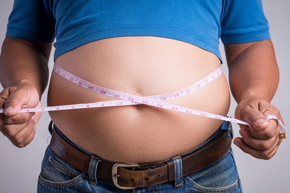 Overweight or fat adult man in very tight jeans with measuring tape on a gray background. Healthcare, medicine concept.